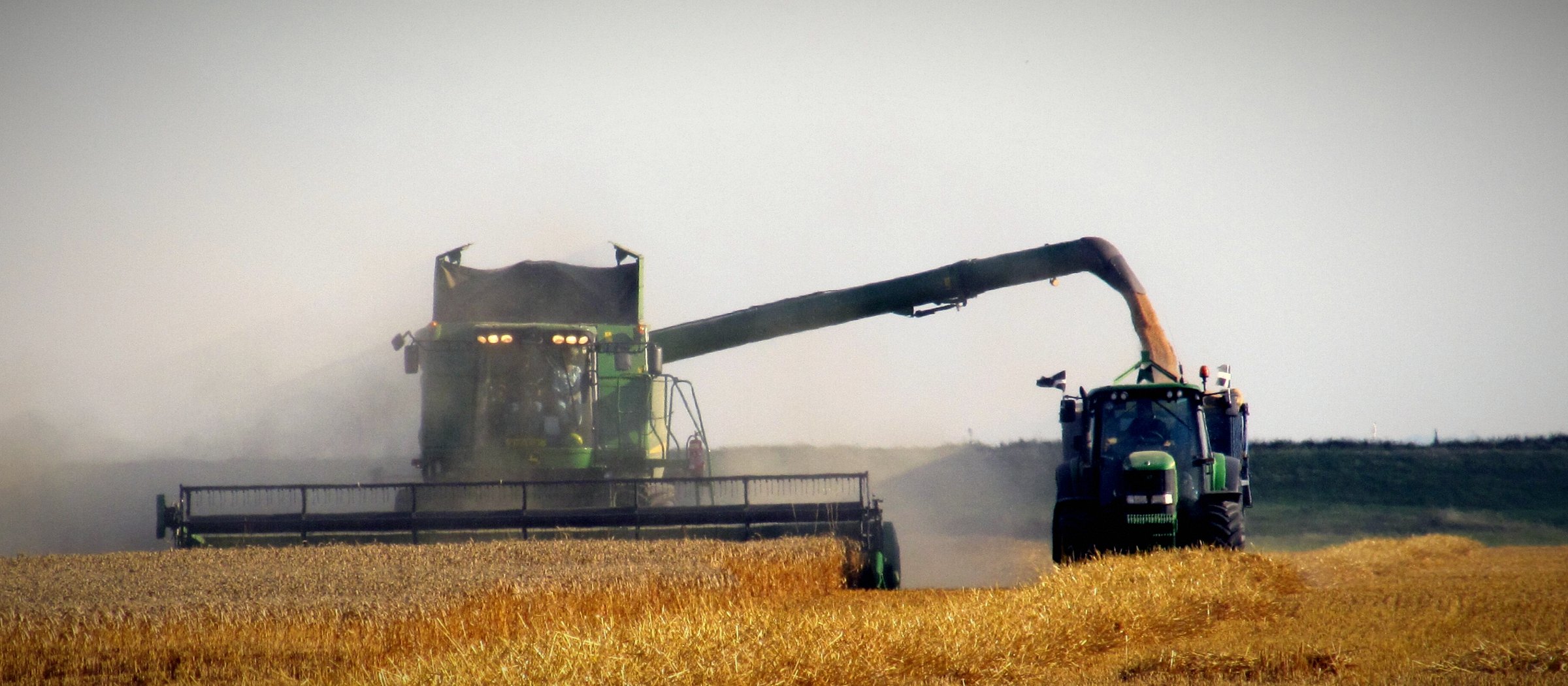 Kombajnë John Deere duke shkarkuar drithin te një traktor gjatë korrjes